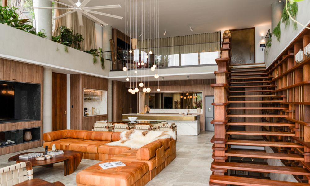 <span class="uk-h4">Stylish open-concept living room with a large leather sectional, modern pendant lighting, floating wooden staircase, and a sleek kitchen in the background.</span>