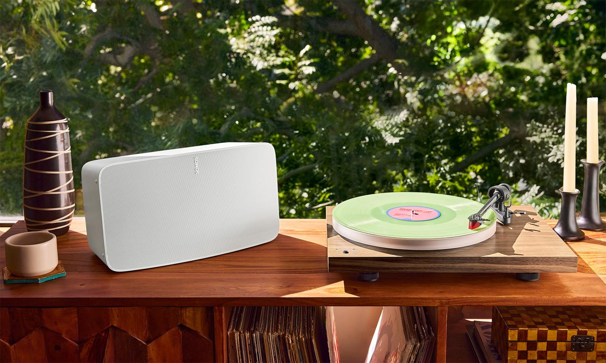 White wireless speaker next to a record player and vinyl setup on a wooden table