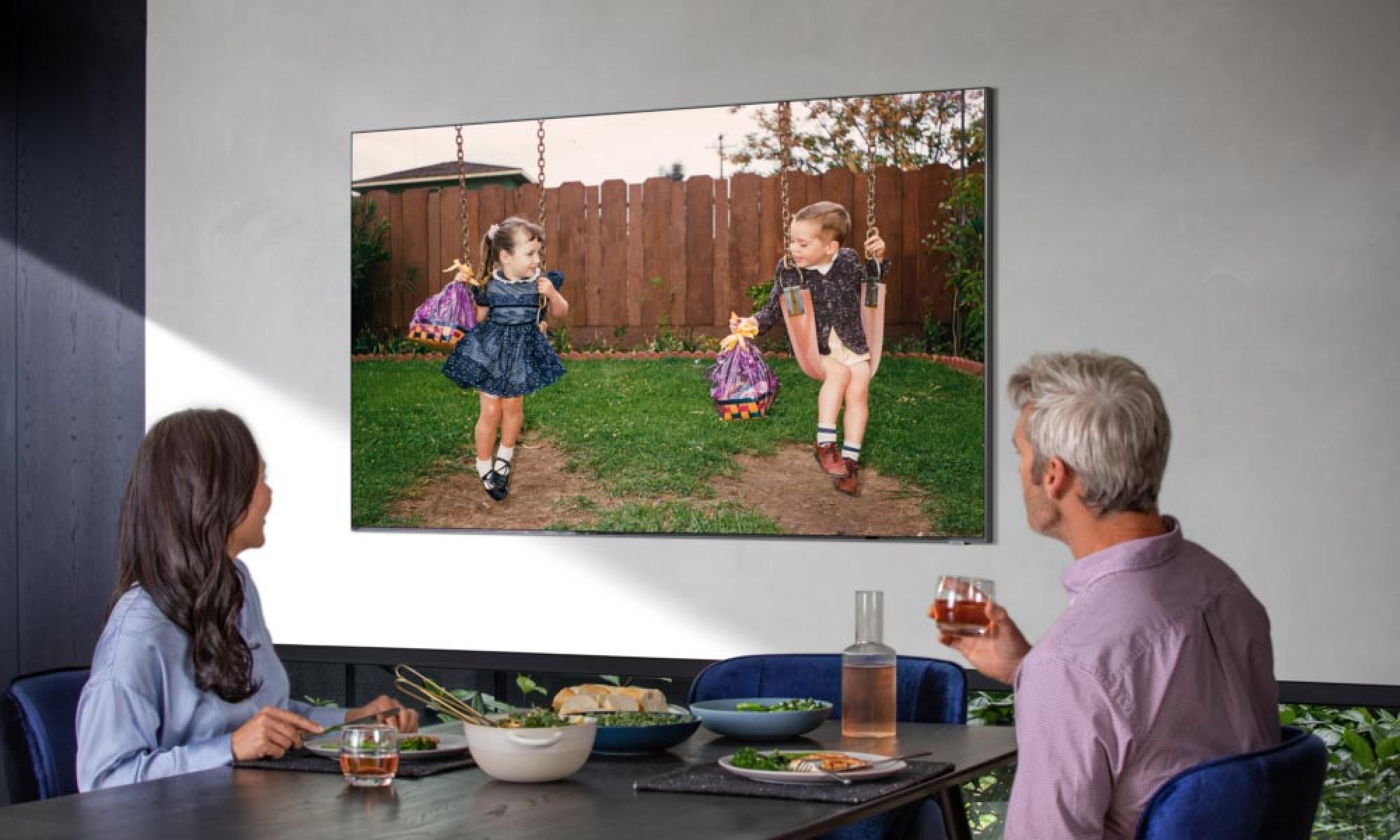 Couple enjoying a meal while watching a TV mounted on a light-colored wall