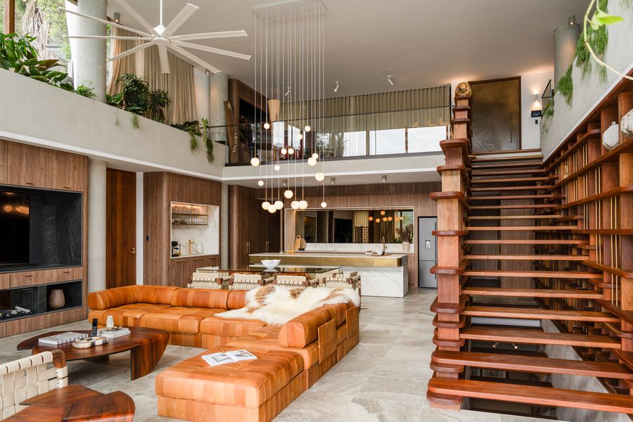 Stylish open-concept living room with a large leather sectional, modern pendant lighting, floating wooden staircase, and a sleek kitchen in the background.